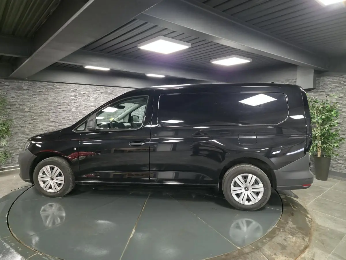 Vue de profil côté gauche d'un Volkswagen Caddy Cargo noir avec jantes acier et portes tôlées en intérieur showroom.