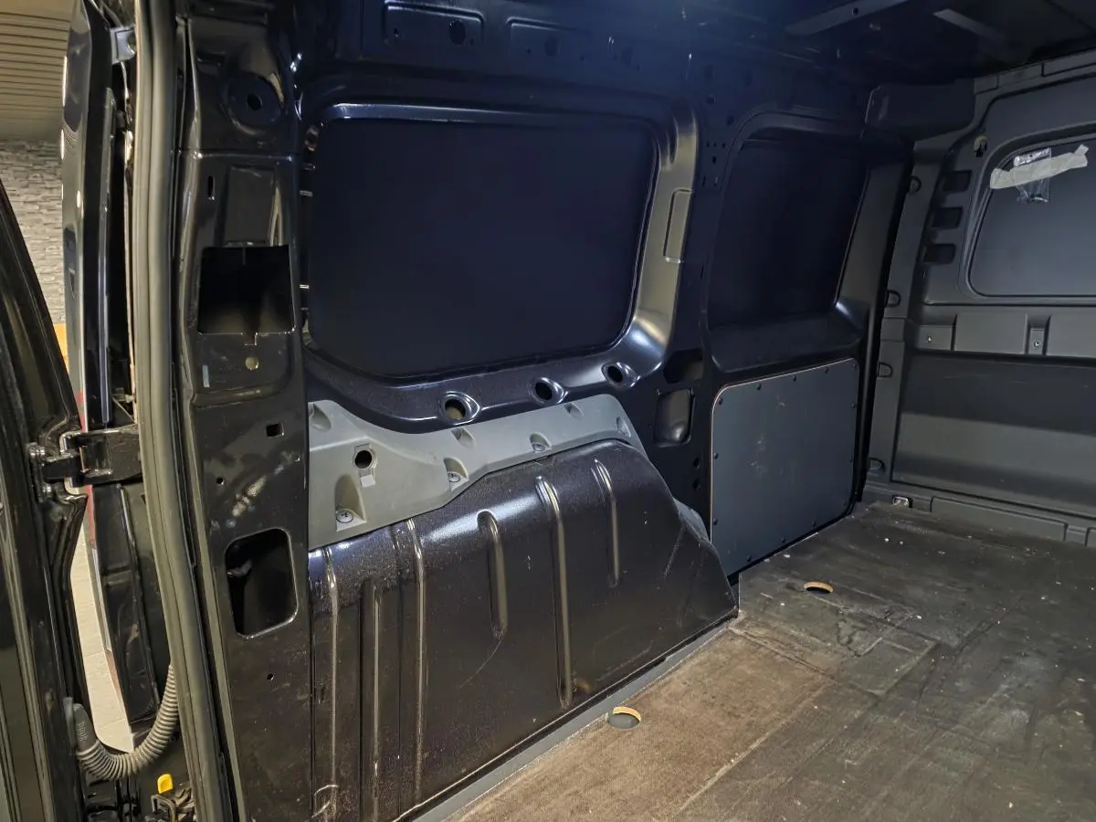 Vue intérieure du compartiment de charge noir du Volkswagen Caddy Cargo 2024, montrant les parois métalliques et le plancher.