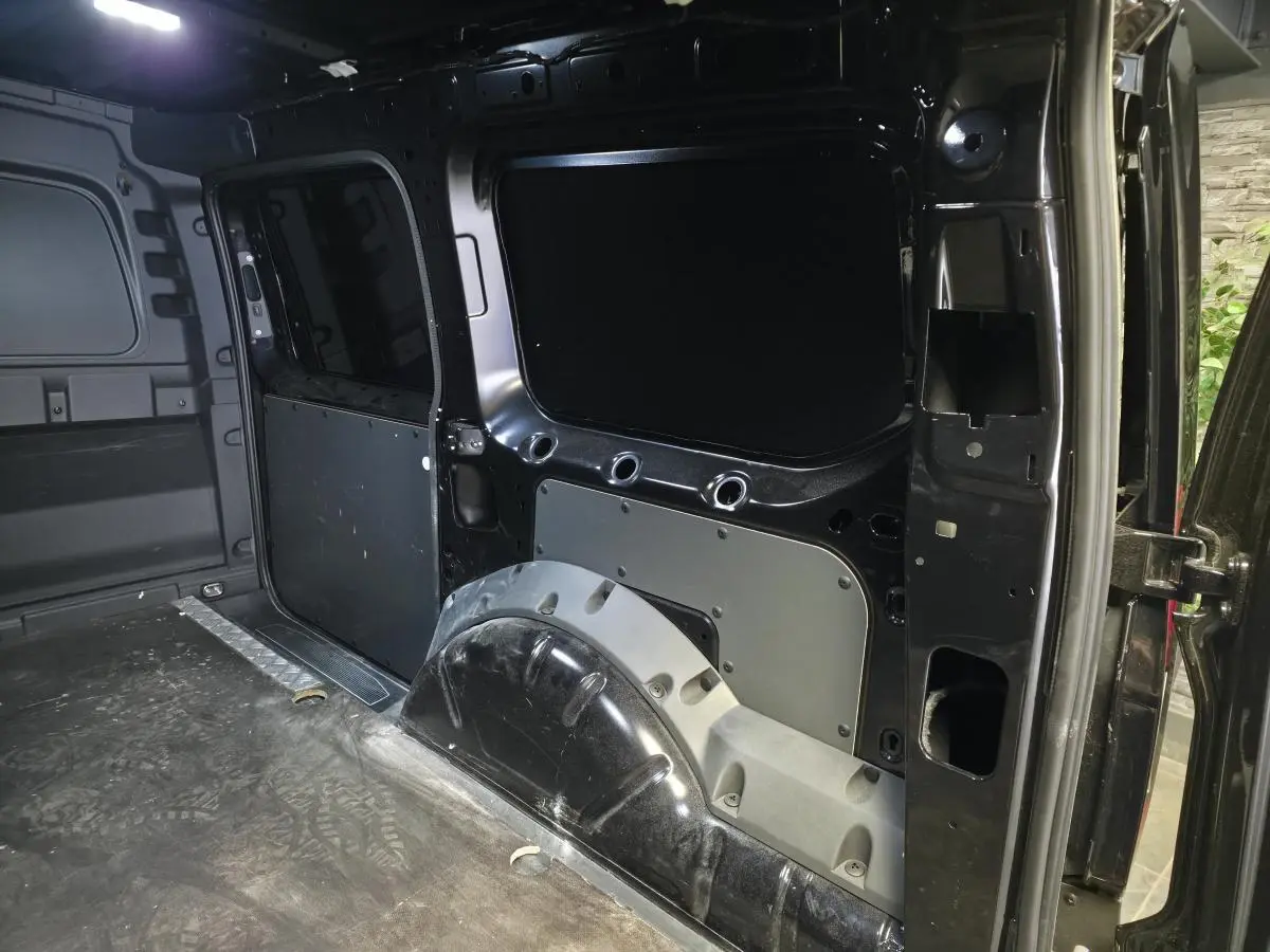 Vue intérieure arrière droite du Volkswagen Caddy Cargo noir 2024, montrant l'espace de chargement tôlé et le passage de roue.
