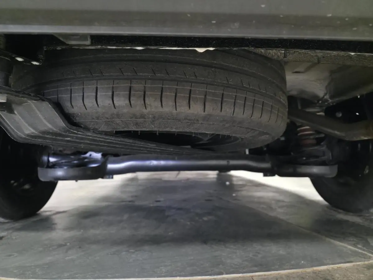 Vue rapprochée sous un Volkswagen Caddy noir 2024 montrant la roue de secours et la suspension arrière.