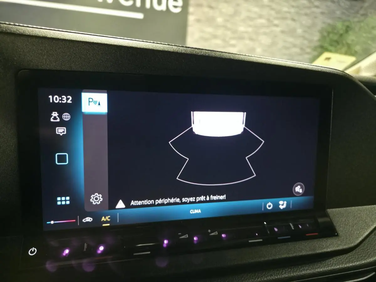 Écran tactile intérieur du Volkswagen Caddy Cargo noir 2024 montrant l'alerte de détection périphérique au stationnement.