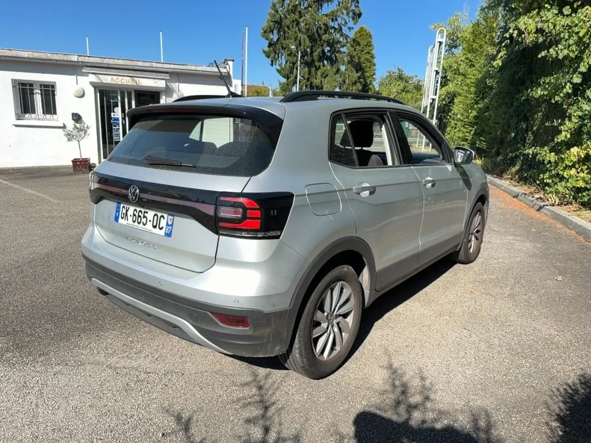 Volkswagen T-Cross gris clair vu en 3/4 arrière droit, avec feux arrière LED et toit noir contrasté.