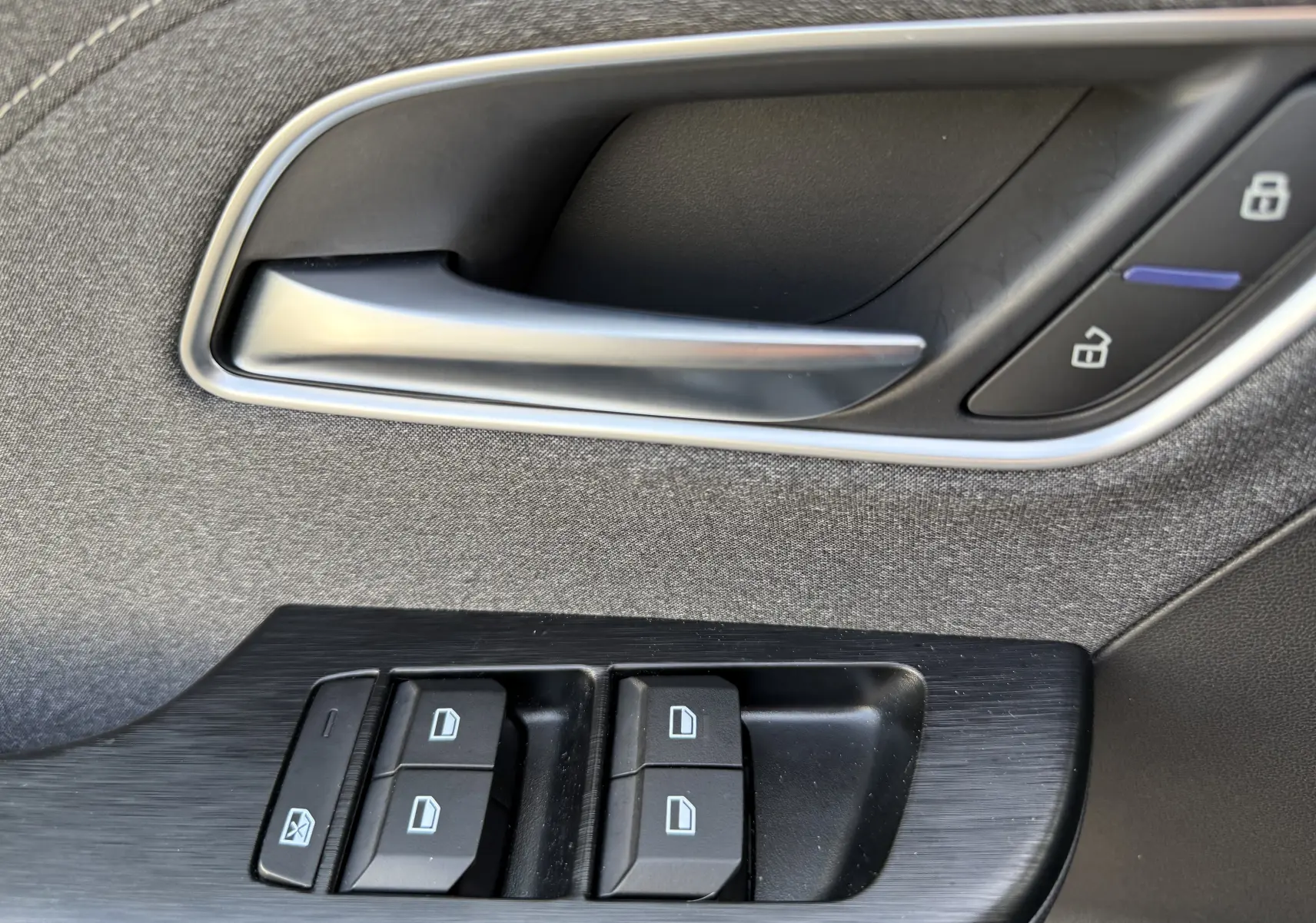 Gros plan sur la poignée intérieure noire et les commandes de lève-vitres du côté gauche d’un MG MOTOR ZS Hybrid 2026.