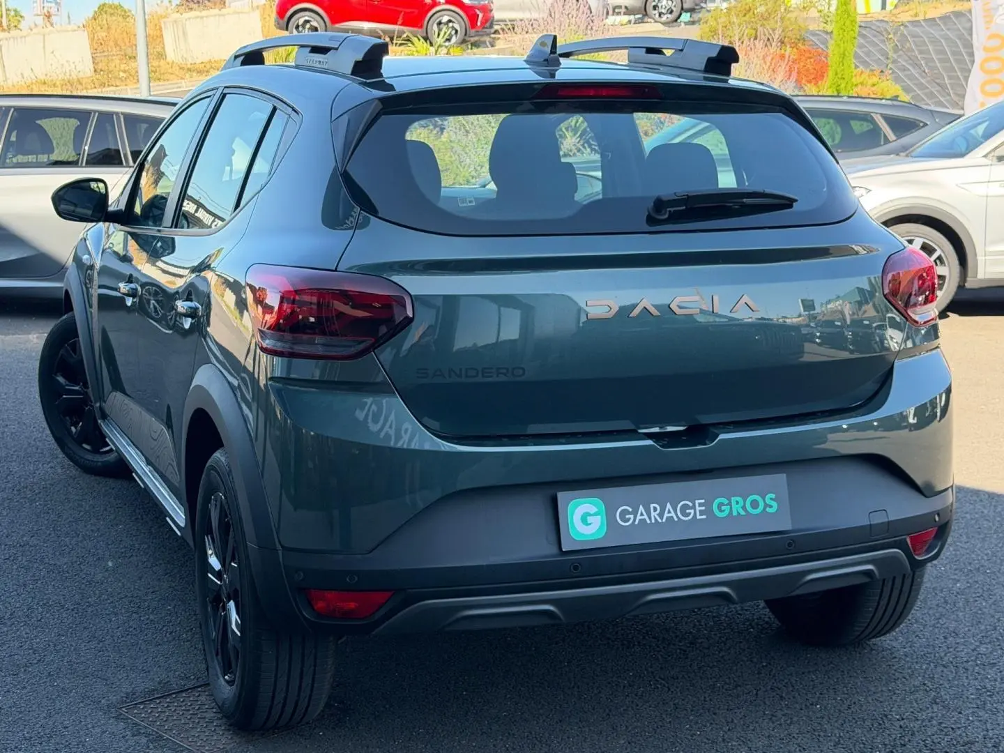 Vue 3/4 arrière droite d'une Dacia Sandero Stepway 2025 vert cèdre métallisé avec barres de toit et jantes noires.