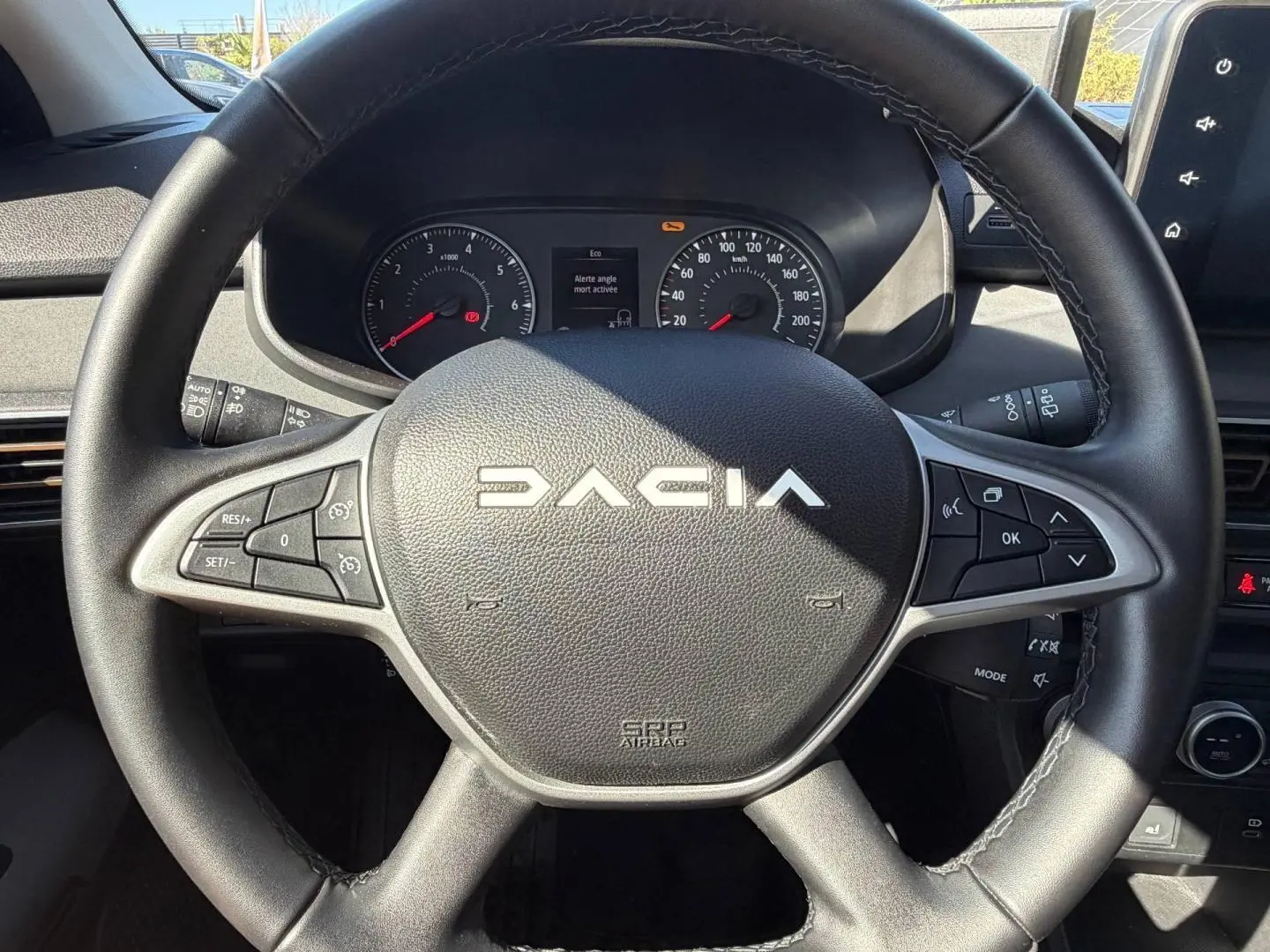 Vue rapprochée du volant noir DACIA avec commandes intégrées et tableau de bord visible en arrière-plan.
