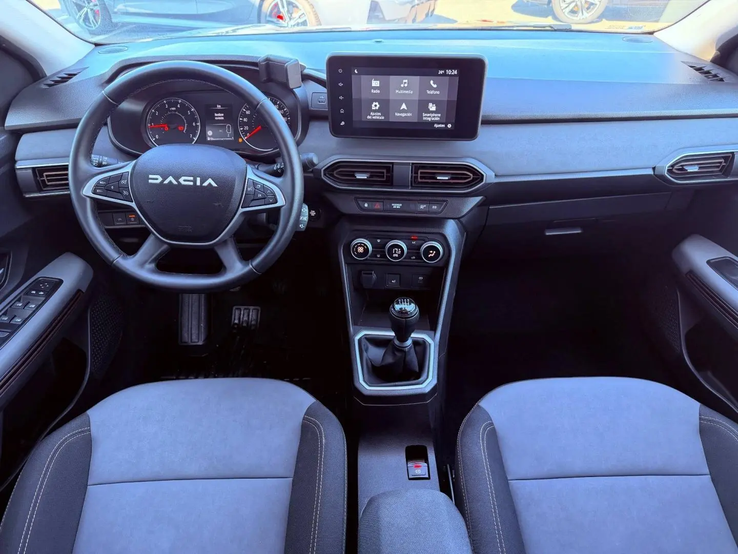 Vue intérieure avant du tableau de bord et volant noir de la Dacia Sandero 2025 avec écran tactile et boîte manuelle.