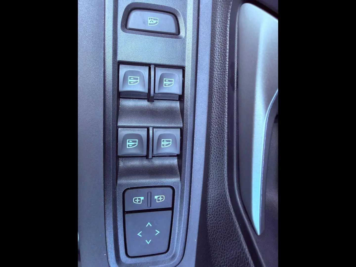 Gros plan sur les commandes de lève-vitres et réglage des rétroviseurs côté conducteur dans une Dacia Sandero 2025.