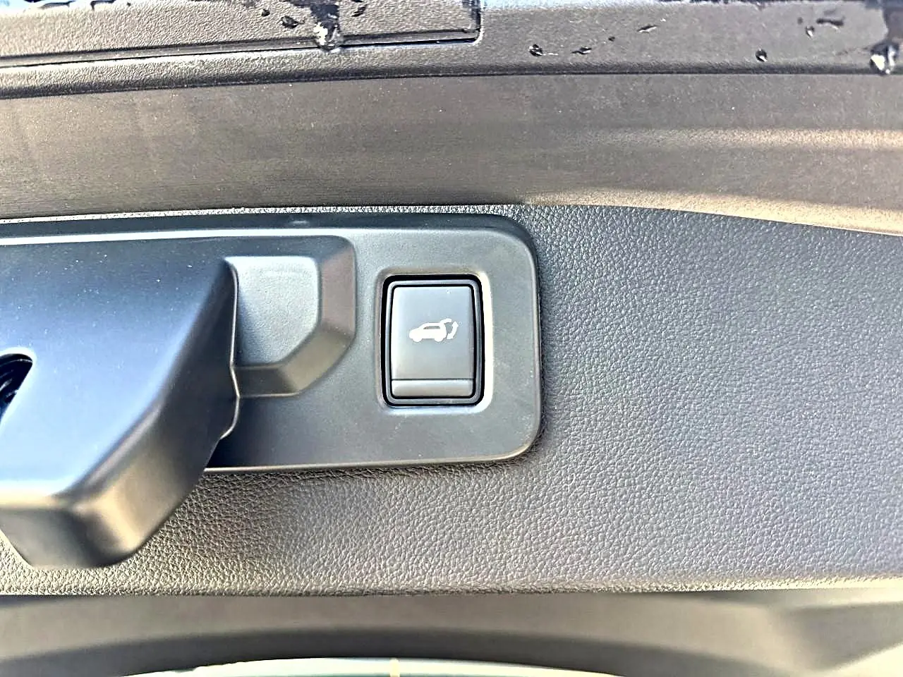 Gros plan sur le bouton d'ouverture électrique du hayon dans le coffre d'une Renault Symbioz gris rafale.