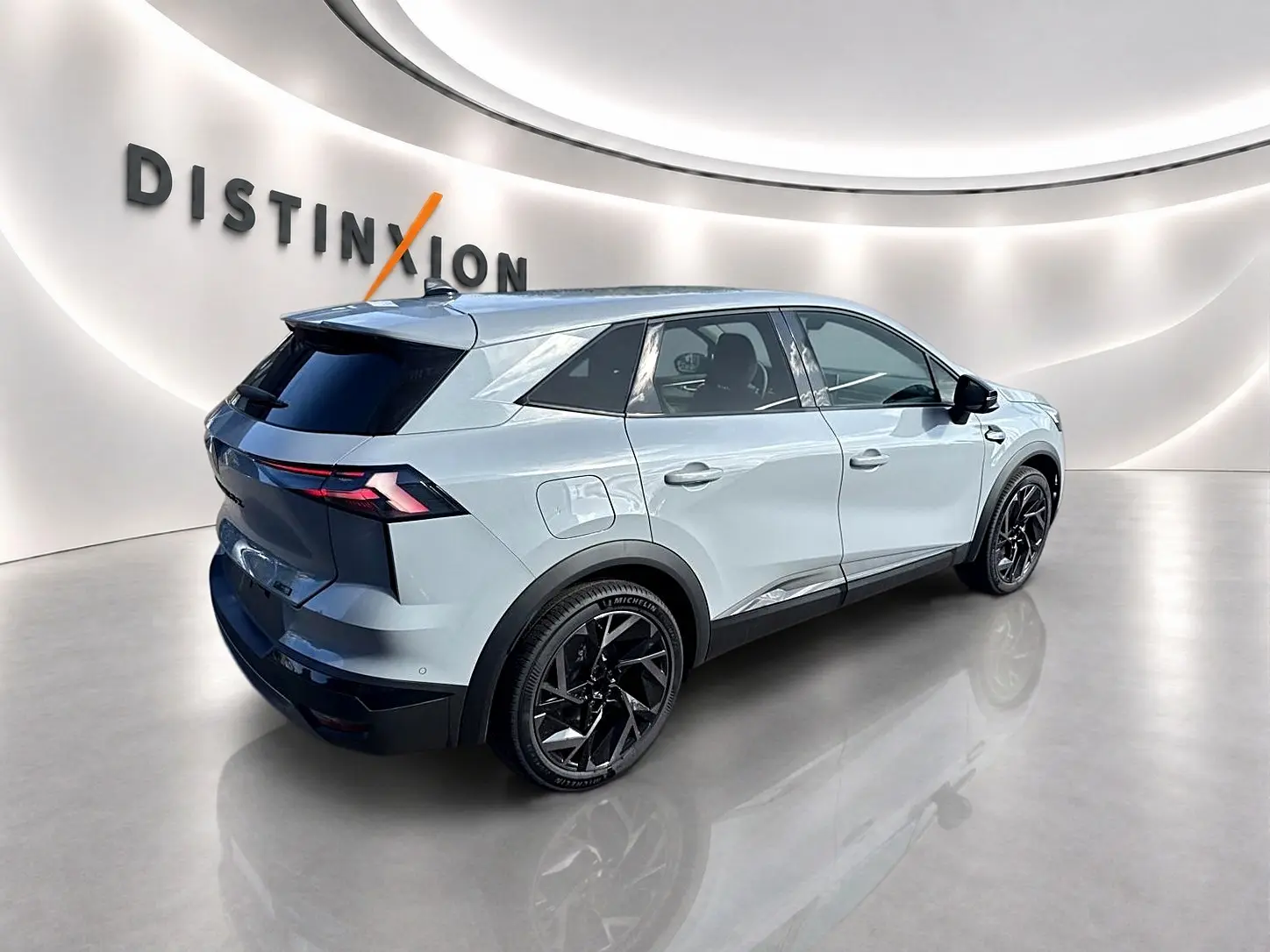 Vue 3/4 arrière droite du Renault Symbioz gris rafale avec jantes noires et feux arrière LED dans un showroom lumineux.