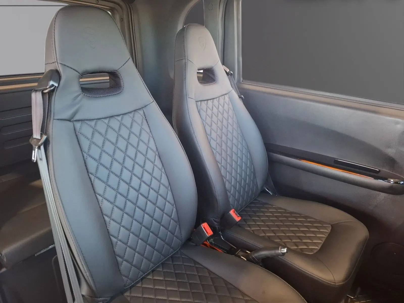 Vue intérieure des sièges avant en cuir noir matelassé du Simplici S1 gris perle avec détails de la portière côté droit.