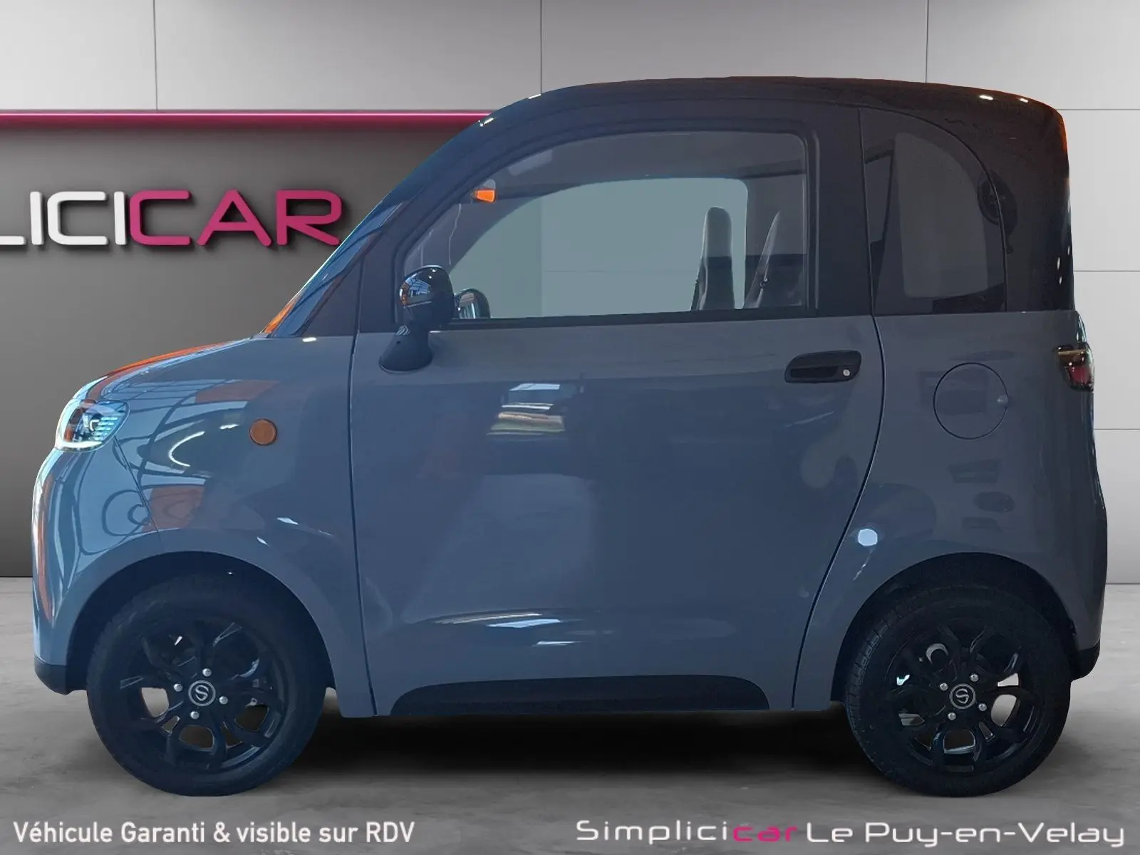 Vue de profil côté gauche d'une Simplici S1 électrique gris perle avec toit noir et jantes noires compactes.