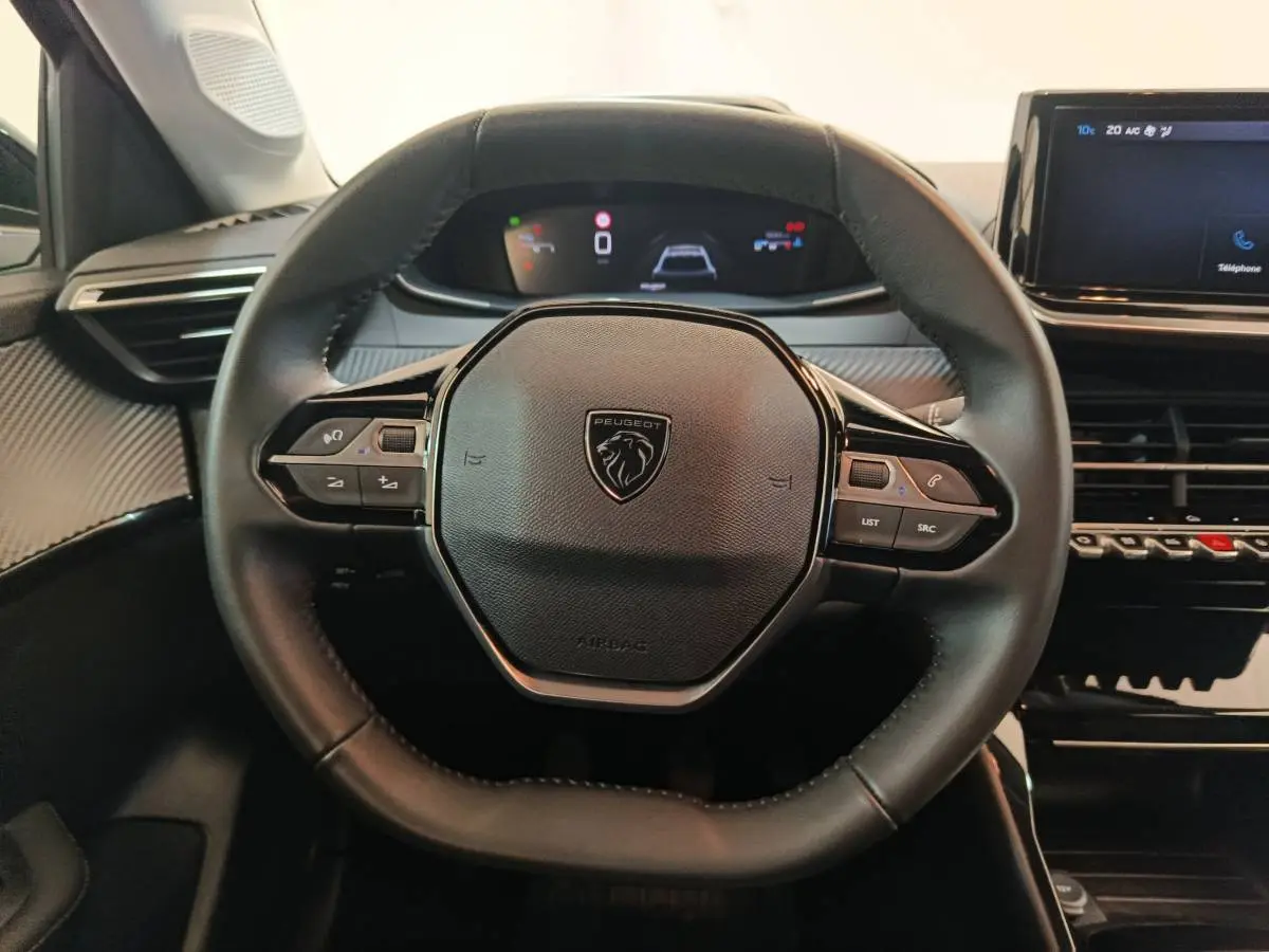 Vue rapprochée du volant cuir multifonctions et du tableau de bord numérique de la Peugeot 208 PureTech 100 S&S Allure 2025.