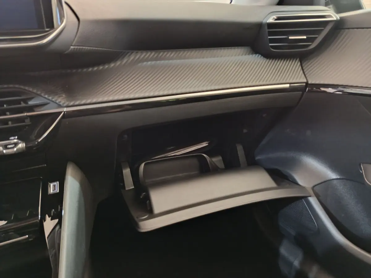 Vue intérieure du tableau de bord gris foncé de la Peugeot 208 PureTech 100 S&S Allure avec boîte à gants ouverte.
