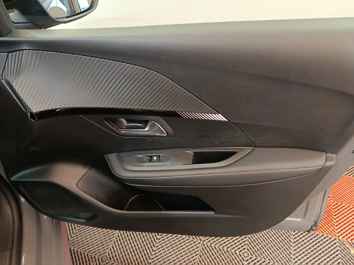 Gros plan sur la porte côté gauche intérieure de la Peugeot 208 gris foncé avec insert carbone et commande de vitre.