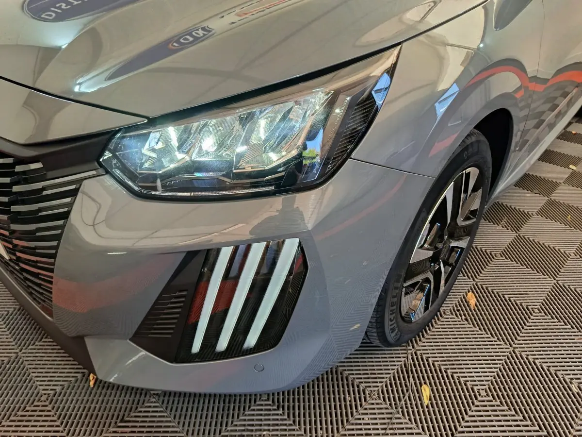 Gros plan sur l'avant droit gris foncé de la Peugeot 208 2025, mettant en valeur ses phares LED et la jante noire.