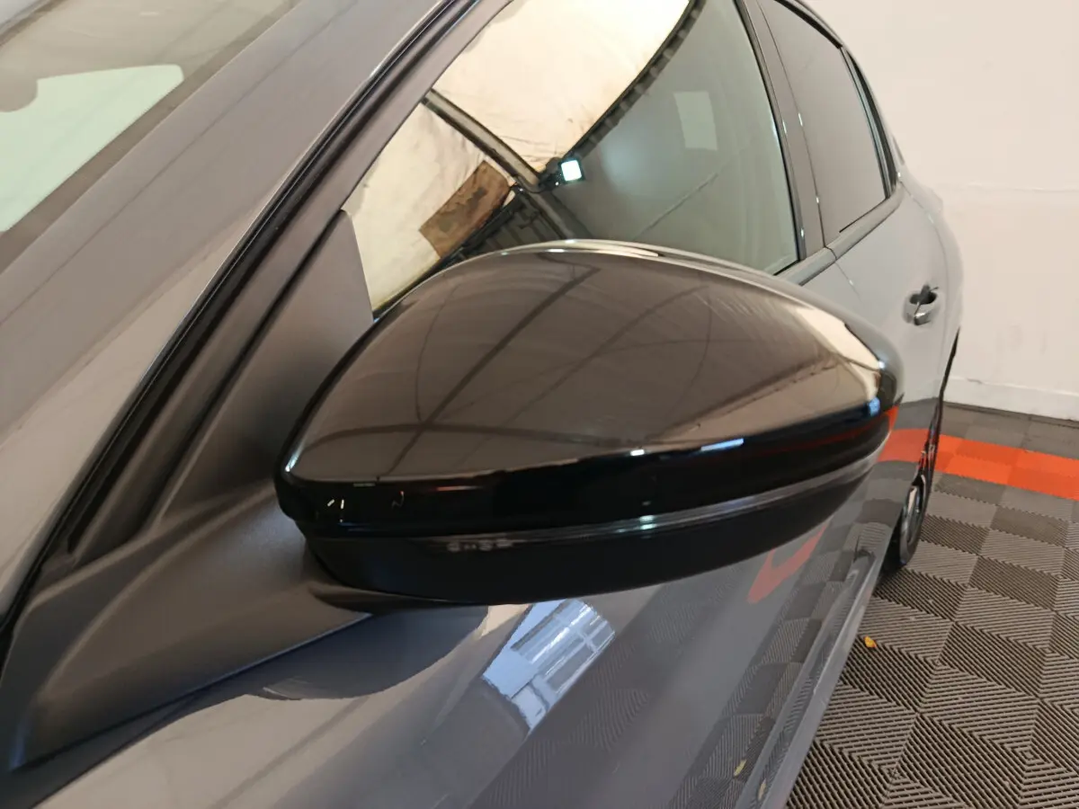 Rétroviseur noir côté gauche sur Peugeot 208 gris foncé, vue rapprochée du profil avant du véhicule.