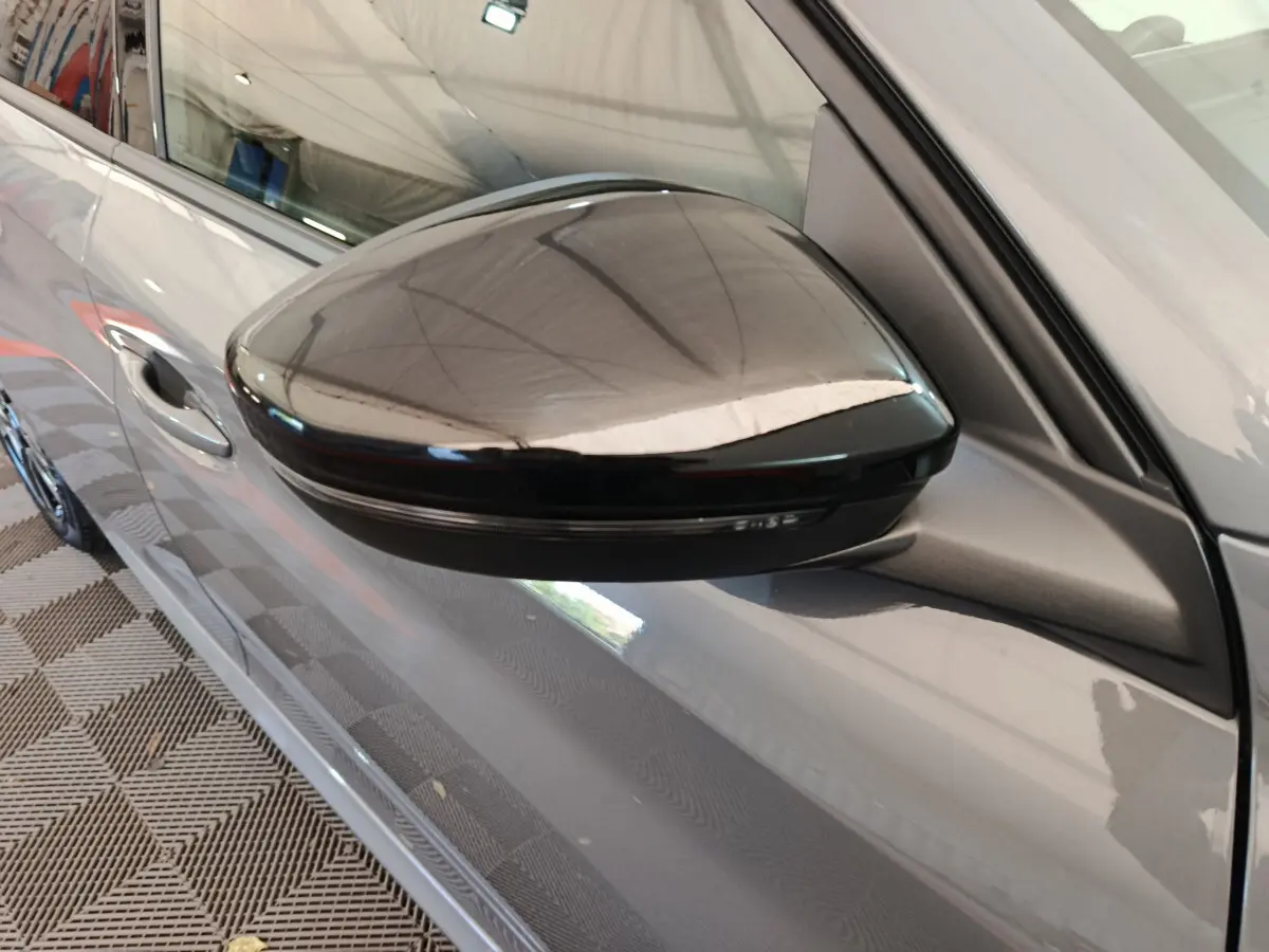 Rétroviseur noir côté gauche d'une Peugeot 208 gris foncé, vue rapprochée en légère plongée.