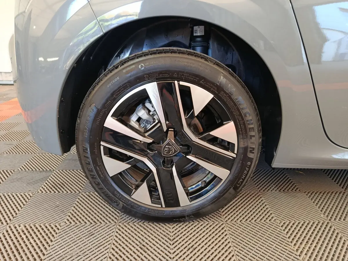 Gros plan sur la roue avant gauche grise d'une Peugeot 208 2025 avec jante alliage bicolore et logo lion central.