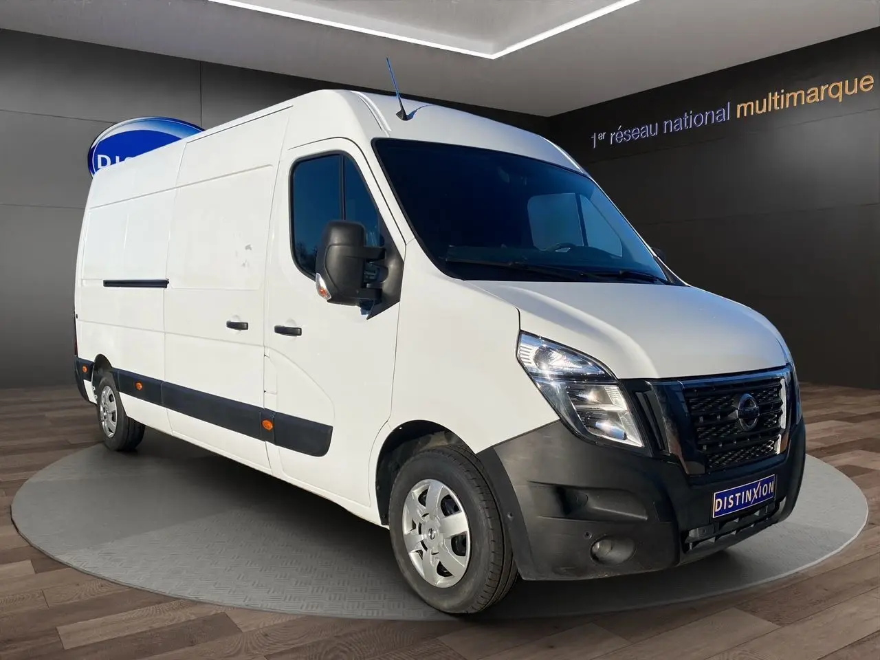 Nissan Interstar blanc en vue 3/4 avant droit, avec pare-chocs noir et rétroviseurs noirs, stationné en intérieur.