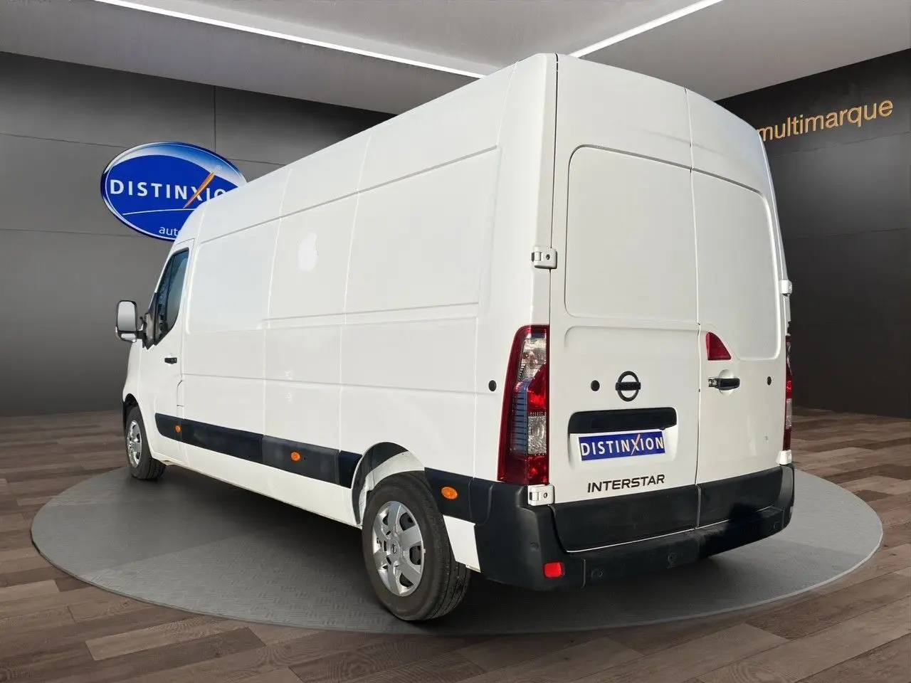 Vue 3/4 arrière droite d’un utilitaire Nissan Interstar blanc avec bande noire latérale et feux arrière verticaux.