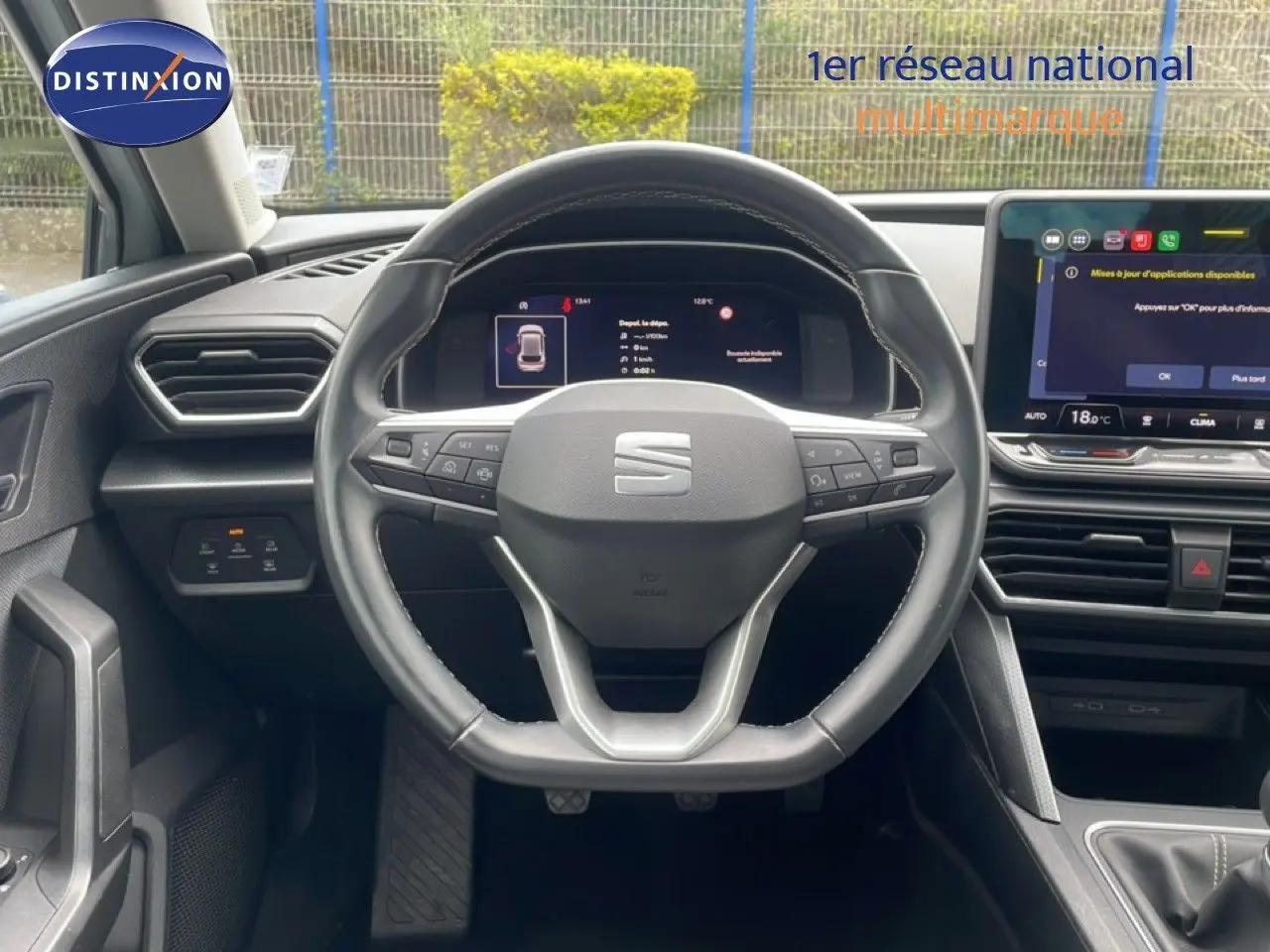 Vue intérieure centrée sur le volant cuir multifonction d'une SEAT Leon blanc neige métal, avec tableau de bord digital et écran tactile.