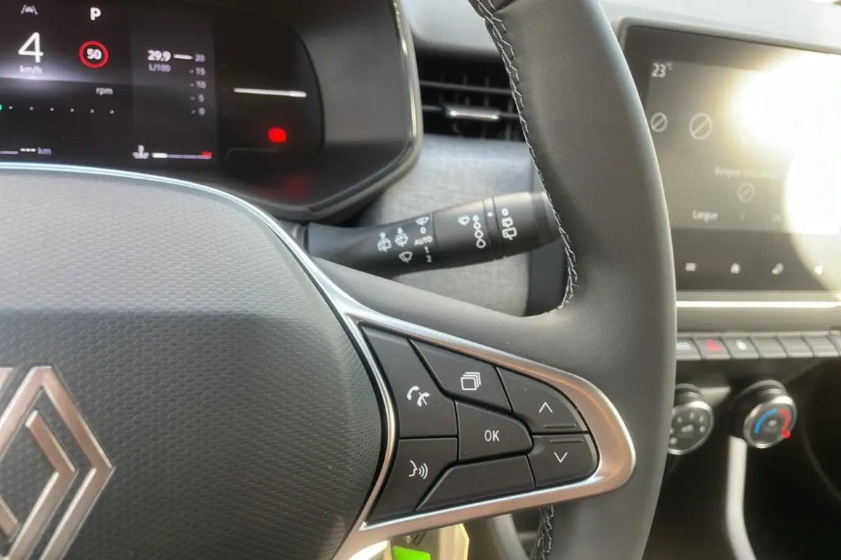 Gros plan sur le volant multifonctions de la Renault Clio gris schiste, avec tableau de bord numérique et commandes intégrées.