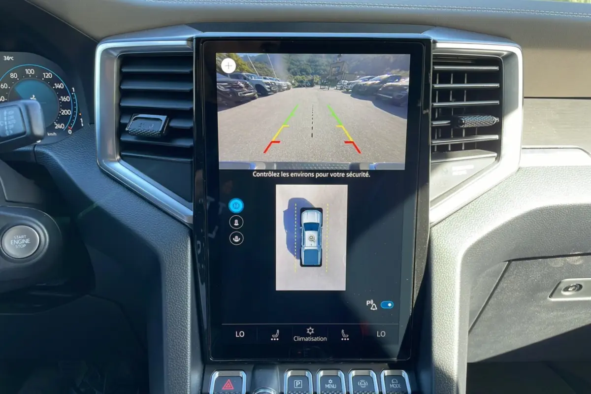 Vue rapprochée de l’écran central tactile du Volkswagen Amarok blanc, affichant la caméra 360° et les réglages de climatisation.