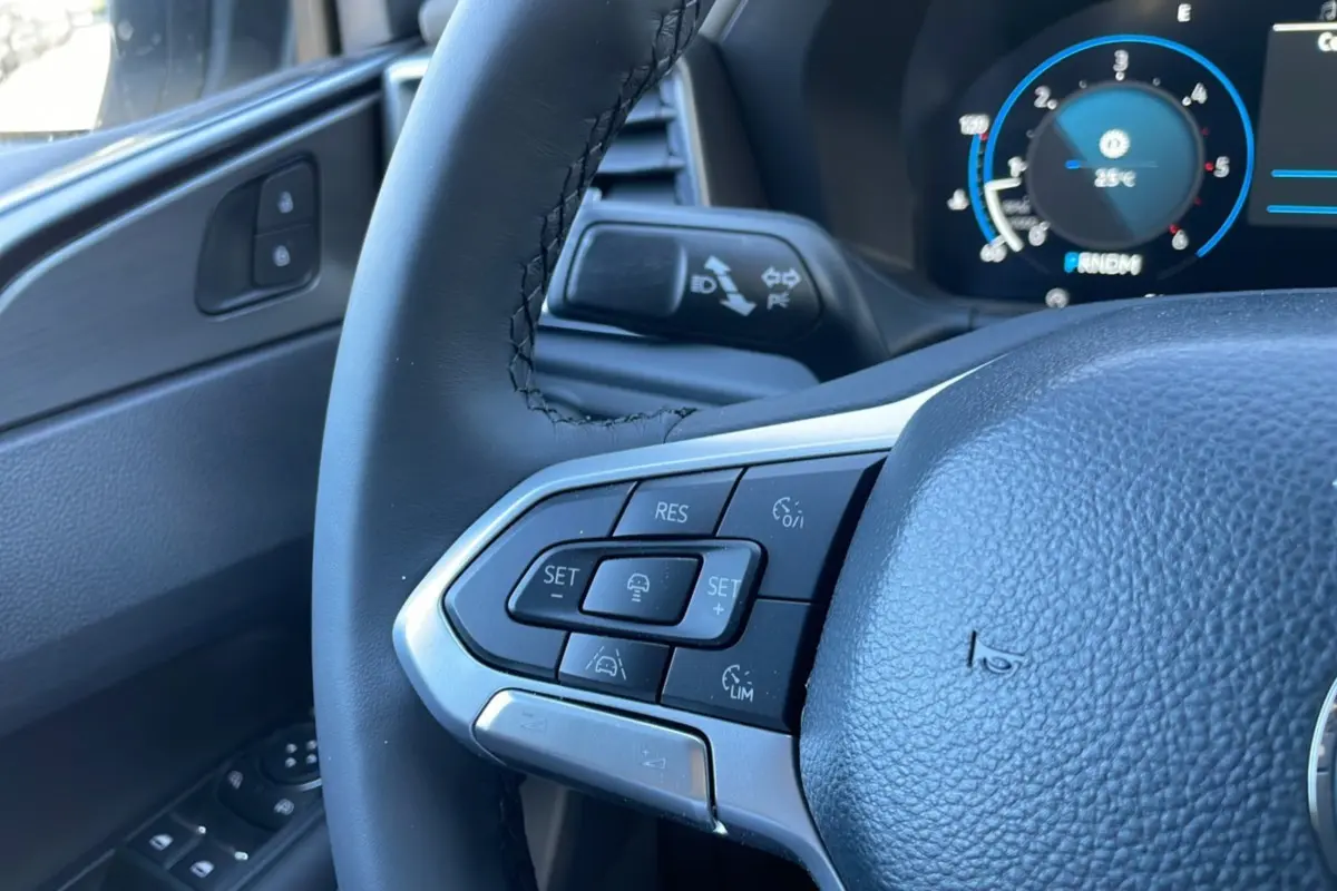 Gros plan sur le volant cuir multifonctions côté gauche du Volkswagen Amarok blanc, avec commandes de régulateur et tableau de bord digital.