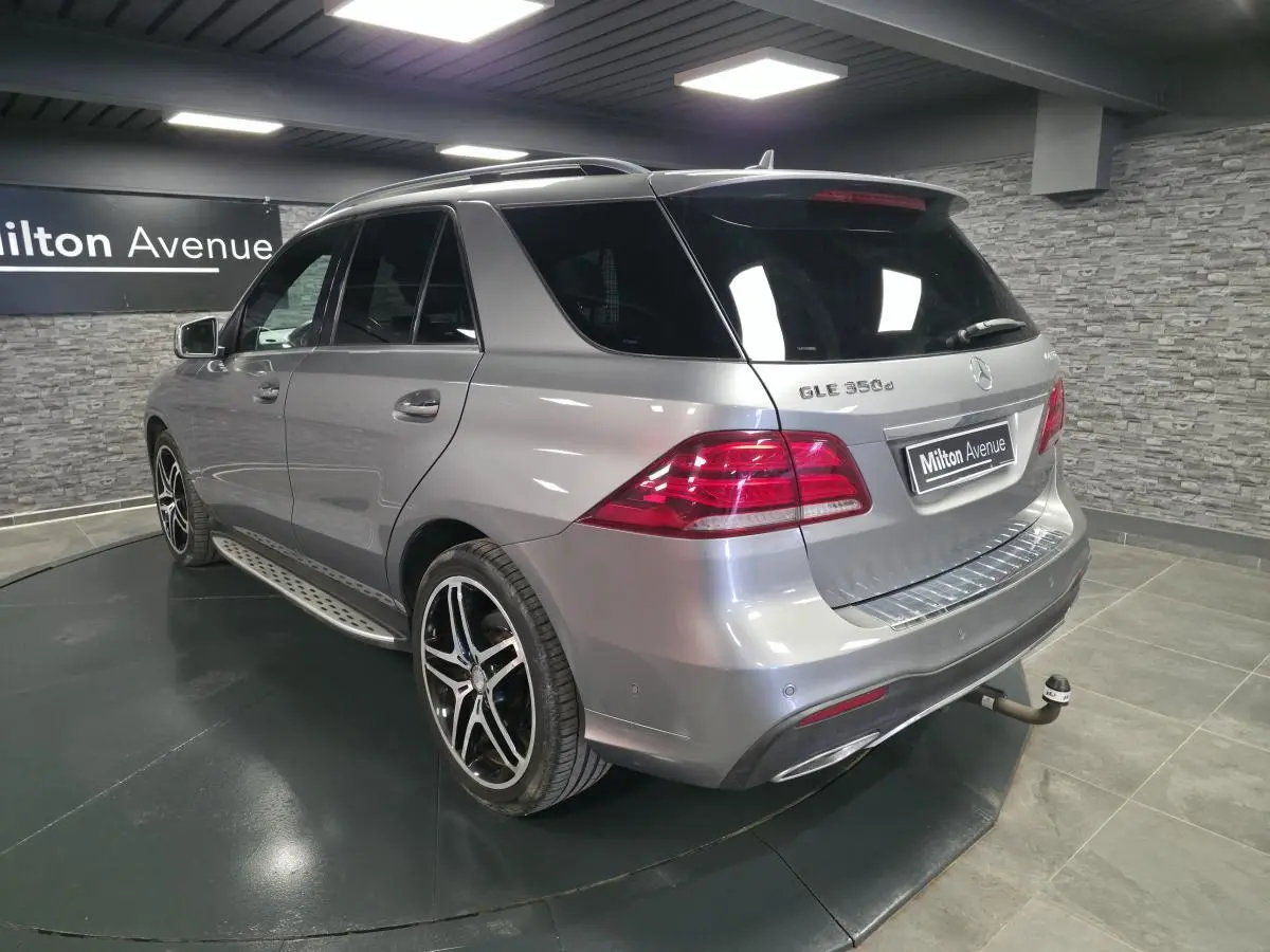 Vue 3/4 arrière droite d'un Mercedes GLE 350 d gris clair avec jantes AMG et attelage démontable en intérieur showroom.