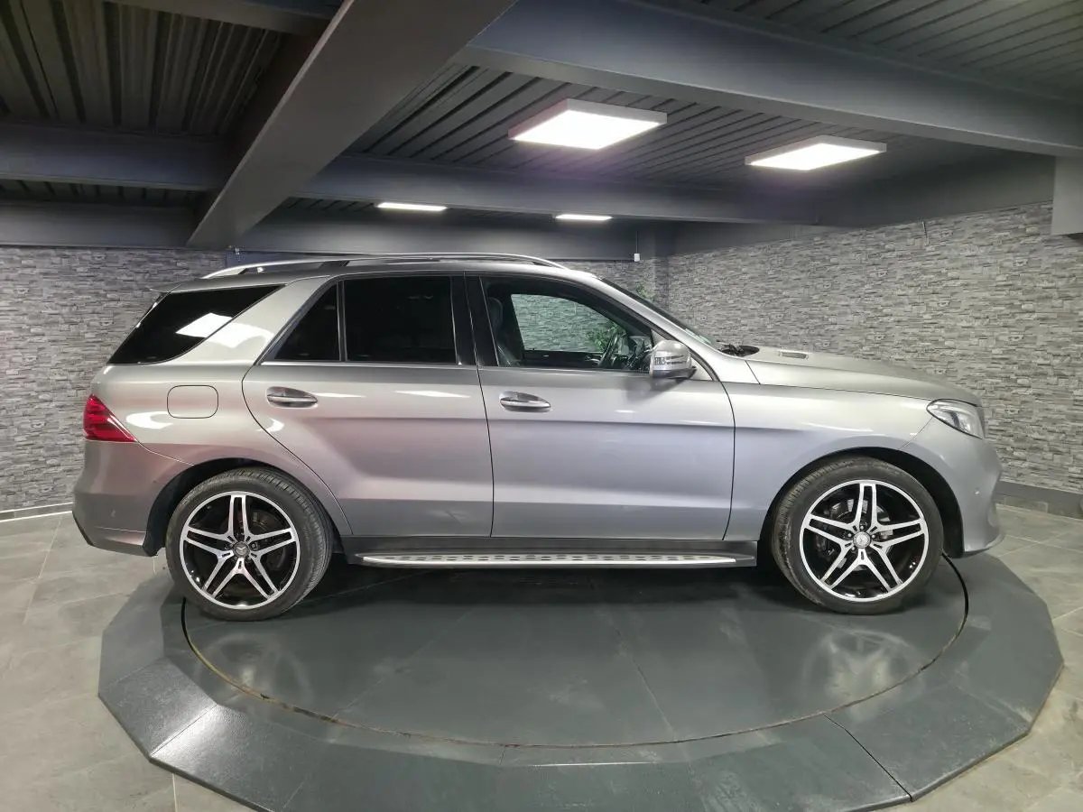 Vue latérale droite d'un Mercedes GLE 350 d gris clair avec jantes AMG 21 pouces et marchepieds inox en intérieur showroom.