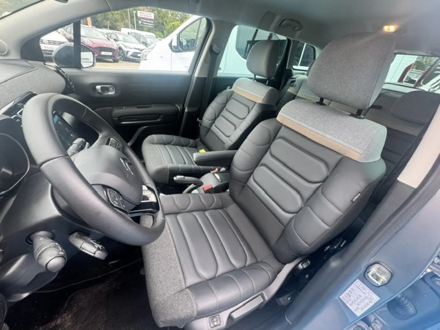 Vue intérieure côté conducteur de la Citroën C3 Aircross 2024, sièges bi-matière gris avec volant cuir noir.