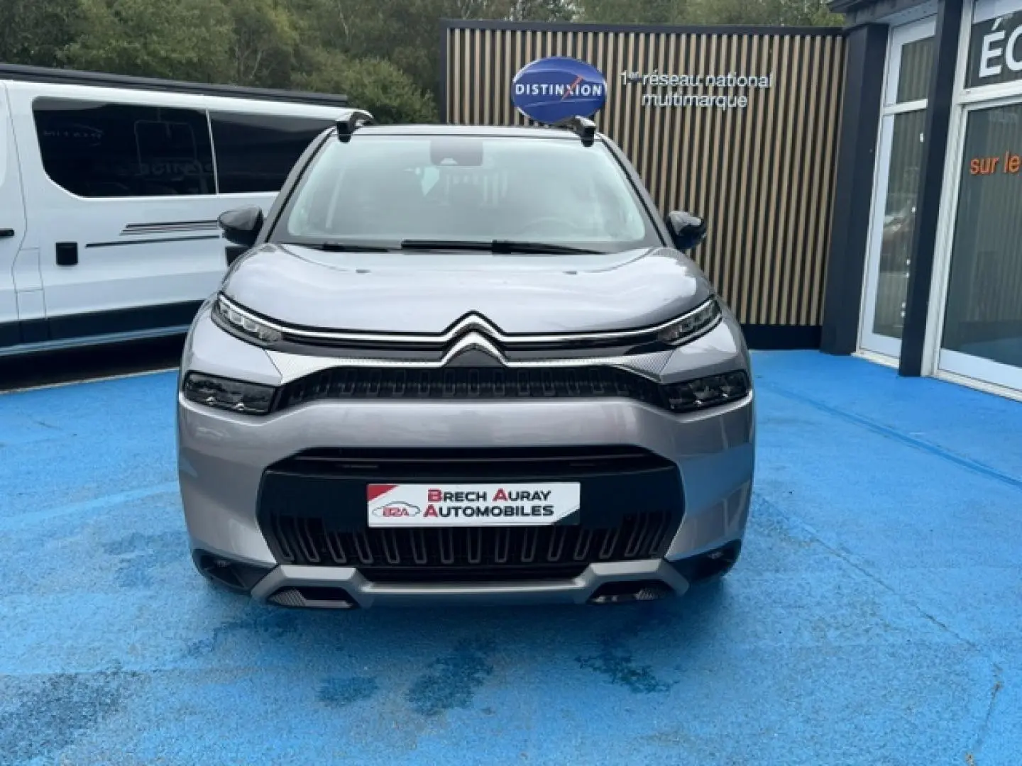 Vue avant d'un Citroën C3 Aircross gris acier 2024 avec calandre noire et barres de toit visibles.