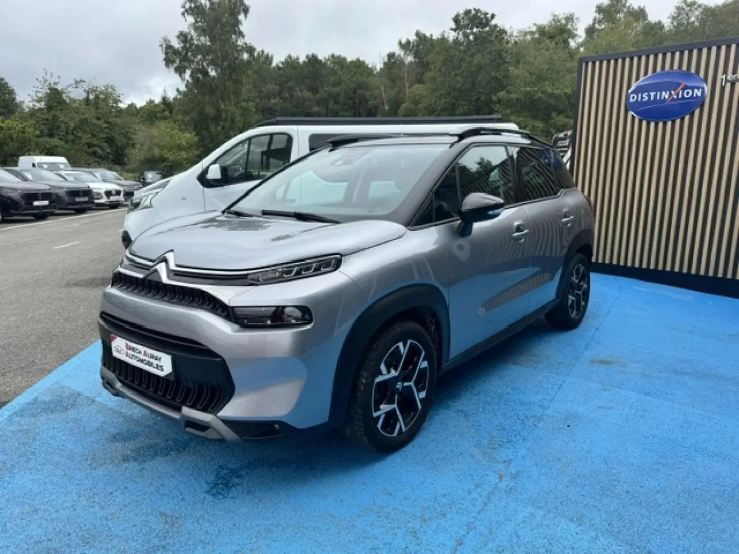 Citroën C3 Aircross gris acier vue 3/4 avant droit, avec barres de toit et jantes alu distinctives.