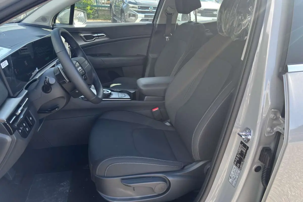 Vue intérieure côté conducteur du Kia Sportage gris céramique 2026, avec sièges tissu noirs et volant cuir multifonctions.