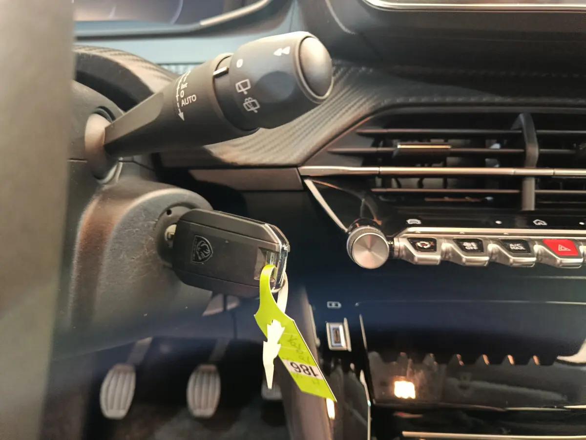 Gros plan sur le tableau de bord noir et la clé insérée dans le contacteur d'une Peugeot 208 gris foncé, version essence manuelle.