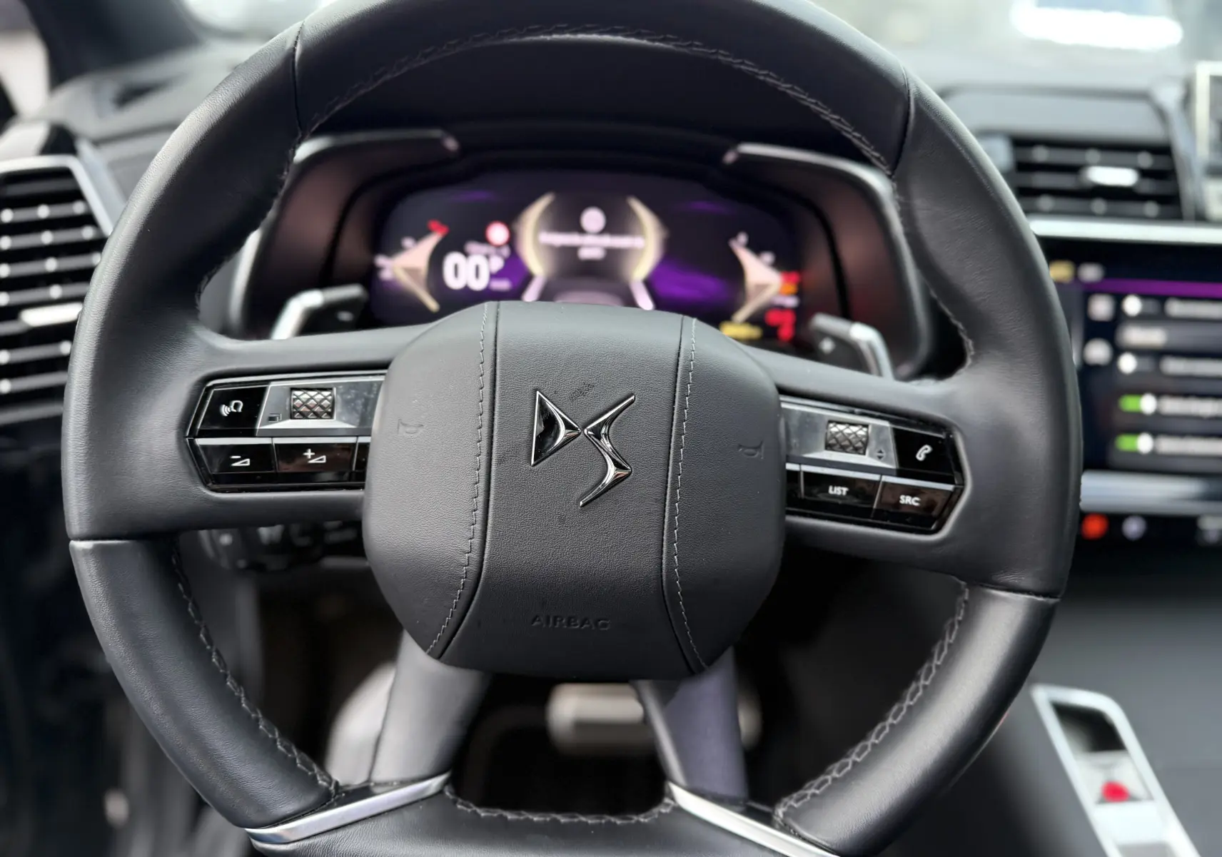 Vue rapprochée du volant en cuir noir du DS7 2025 avec commandes intégrées et tableau de bord numérique en arrière-plan flou.