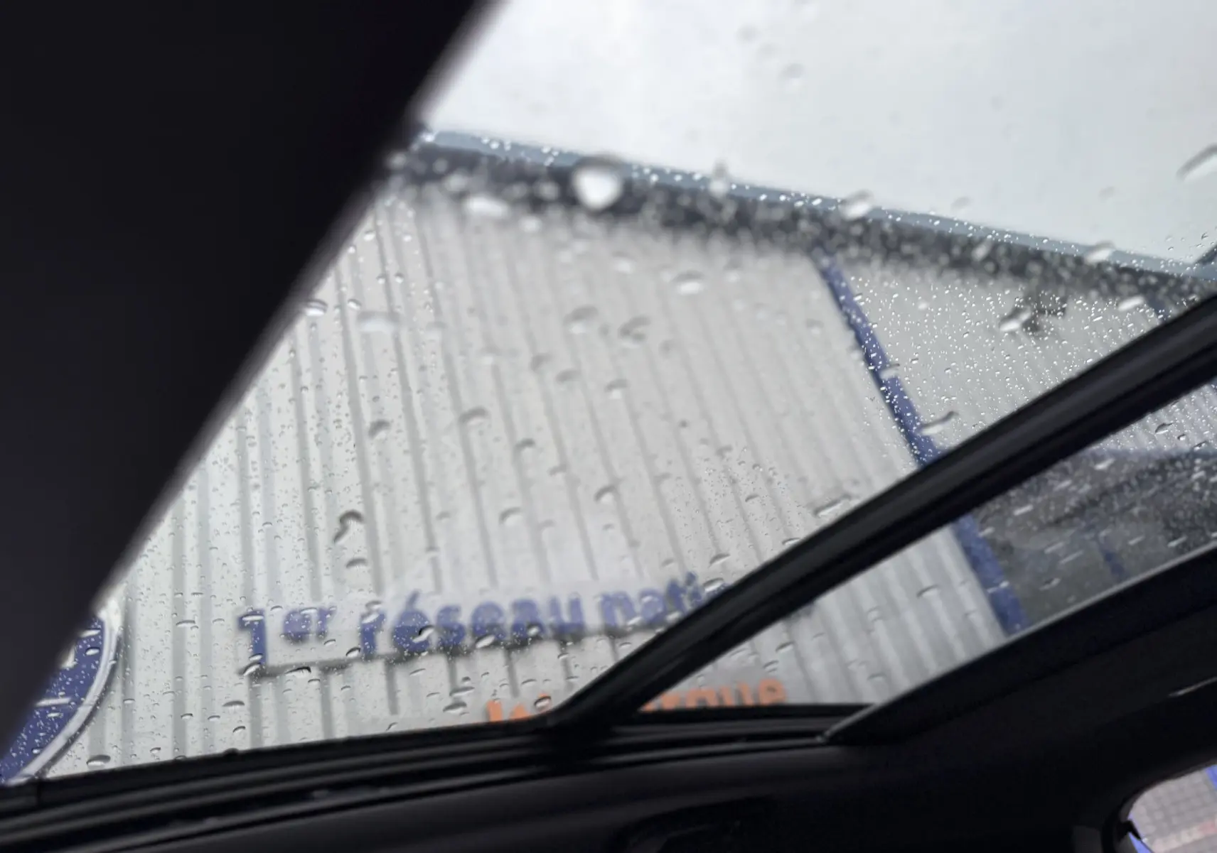 Vue intérieure du toit ouvrant électrique du DS7 gris titane avec gouttes de pluie visibles sur le verre panoramique.