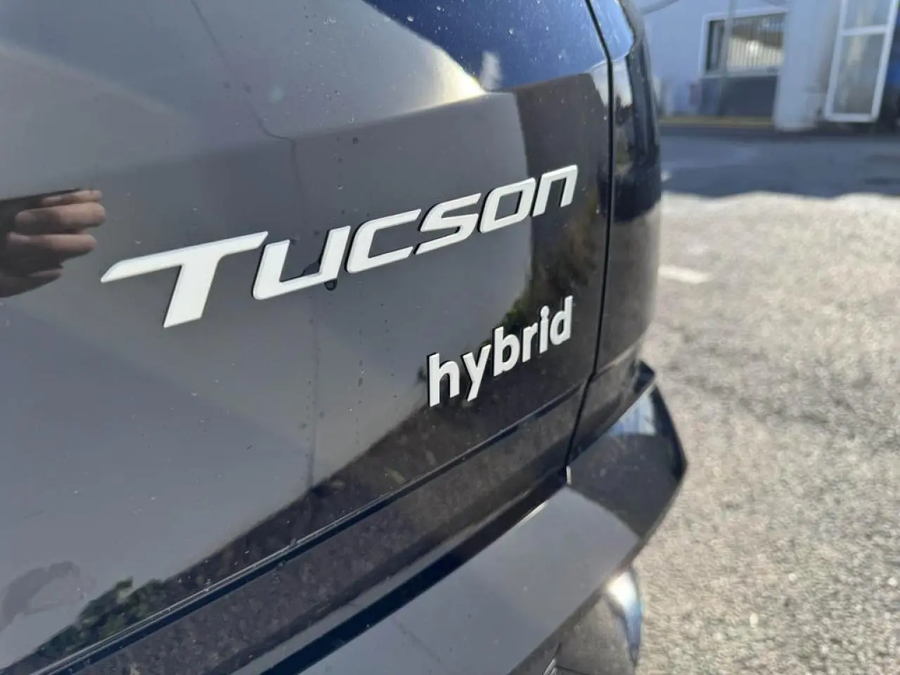 Gros plan sur l'arrière noir abyss métallisé du Hyundai Tucson IV avec badges "Tucson" et "hybrid" visibles.