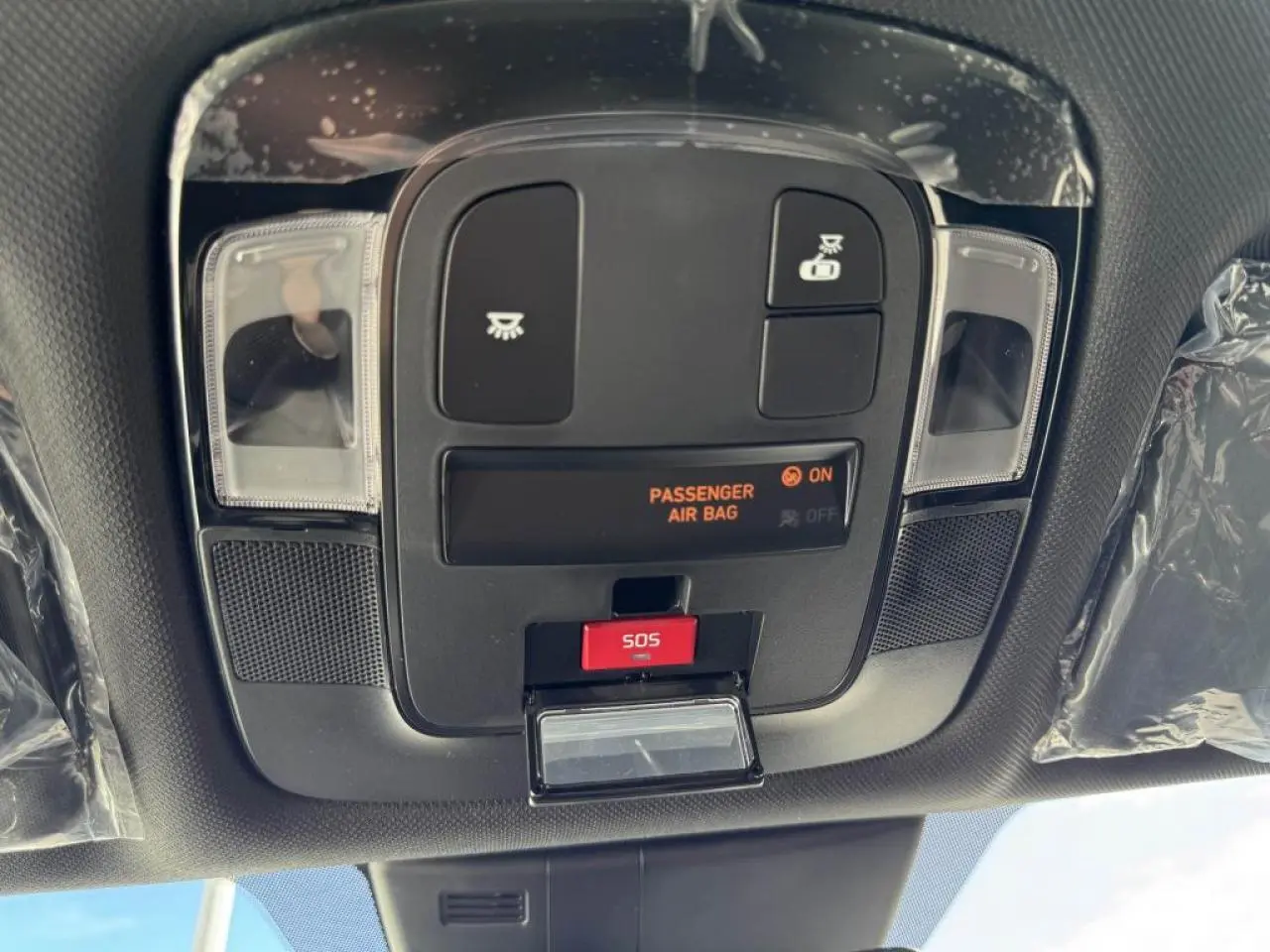 Vue en gros plan du panneau de commandes au plafond du Hyundai Tucson noir avec bouton SOS et indicateur airbag passager.