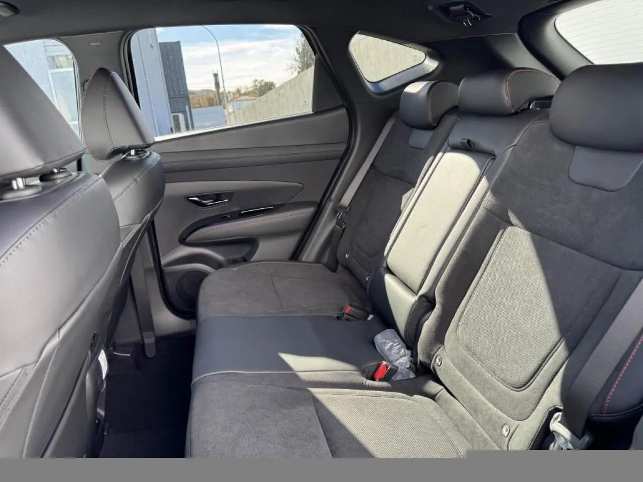Vue intérieure arrière côté droit du Hyundai Tucson 2025 avec sellerie cuir/alcantara noire et surpiqûres rouges.