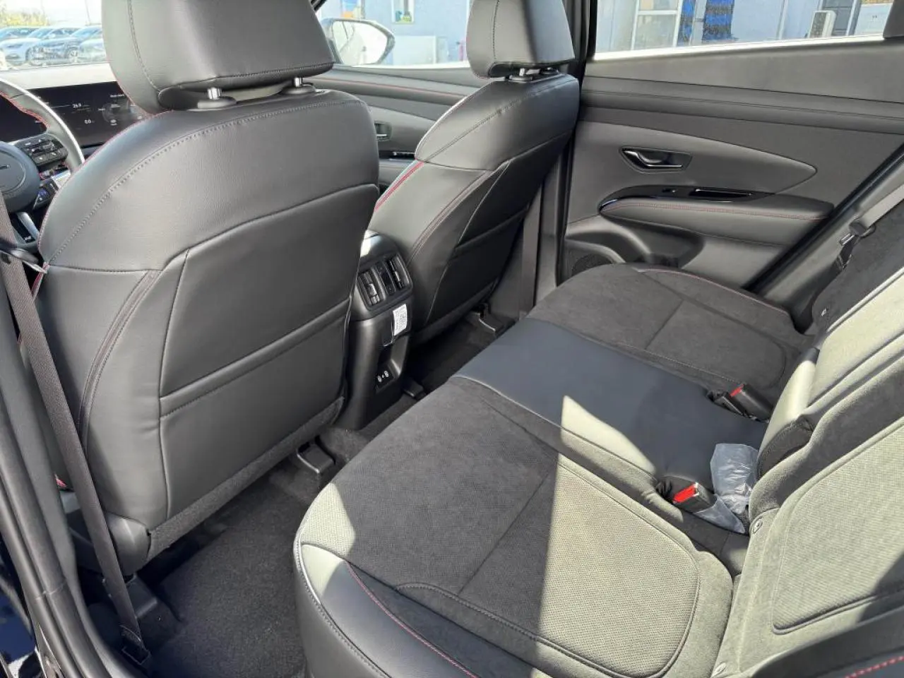Vue arrière intérieure du Hyundai Tucson 2025, sièges cuir/alcantara noirs avec surpiqûres rouges et accoudoir central.