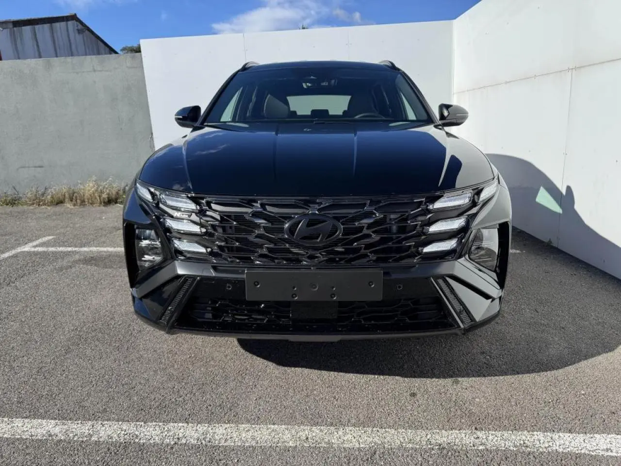 Vue frontale d'un Hyundai Tucson noir Abyss Metal avec calandre noire et phares LED distinctifs, stationné en extérieur.