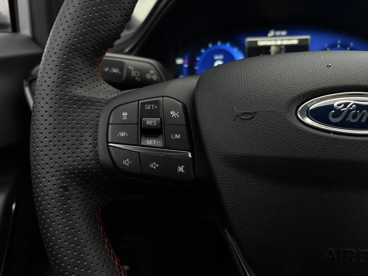 Gros plan sur le volant perforé noir avec surpiqûres rouges du Ford Puma 2023, boutons de commande multifonctions visibles.