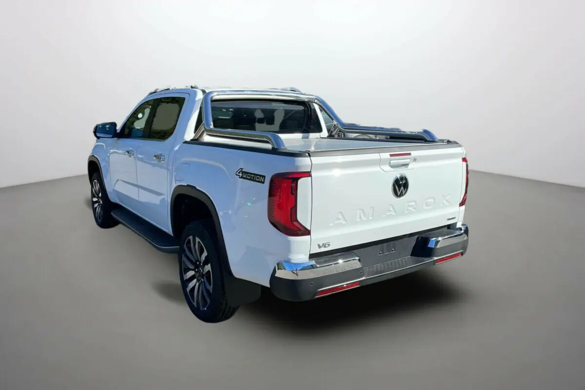 Vue 3/4 arrière droite du Volkswagen Amarok blanc V6 240 BVA10 Aventura avec arceaux inox et jantes alu 21 pouces.