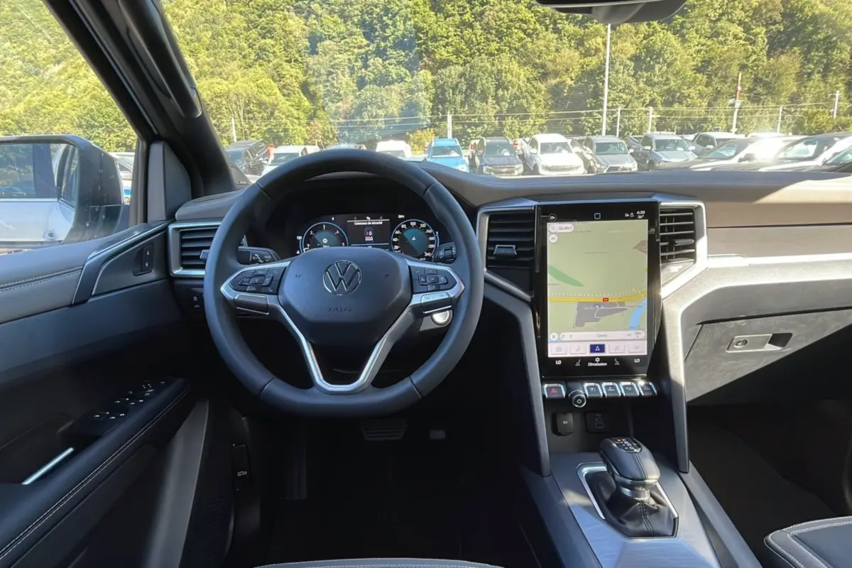 Vue intérieure avant du Volkswagen Amarok blanc 2026, tableau de bord moderne avec écran tactile vertical et volant multifonctions.