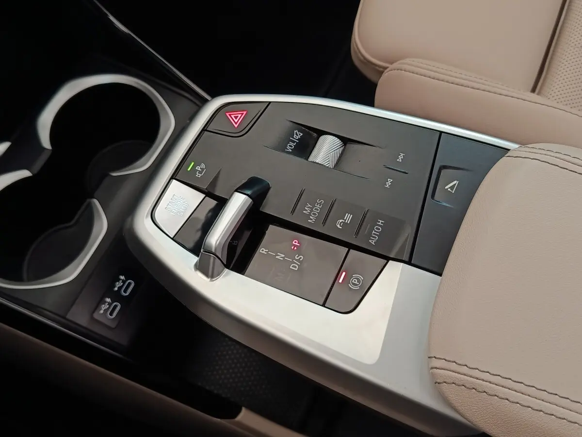 Gros plan sur la console centrale beige du BMW X1 xDrive25e 2024 avec levier de vitesse et commandes tactiles.