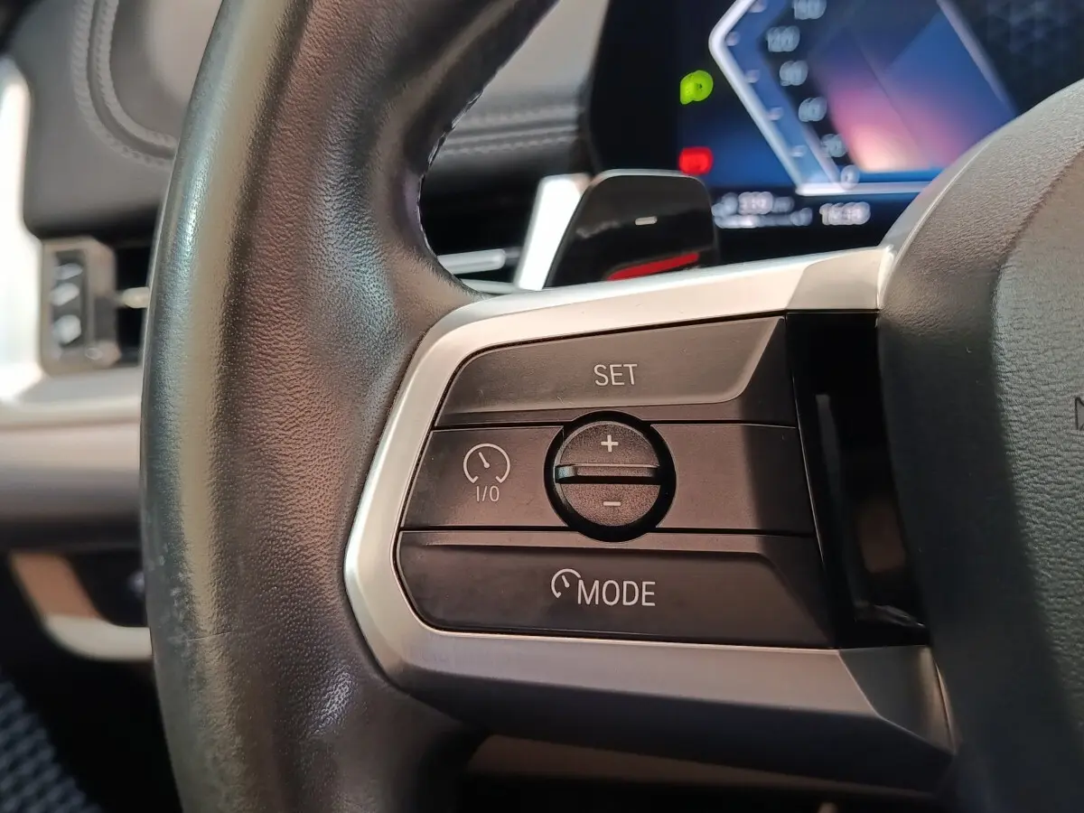 Gros plan sur les commandes du régulateur de vitesse au volant cuir noir du BMW X1 xDrive25e 2024.