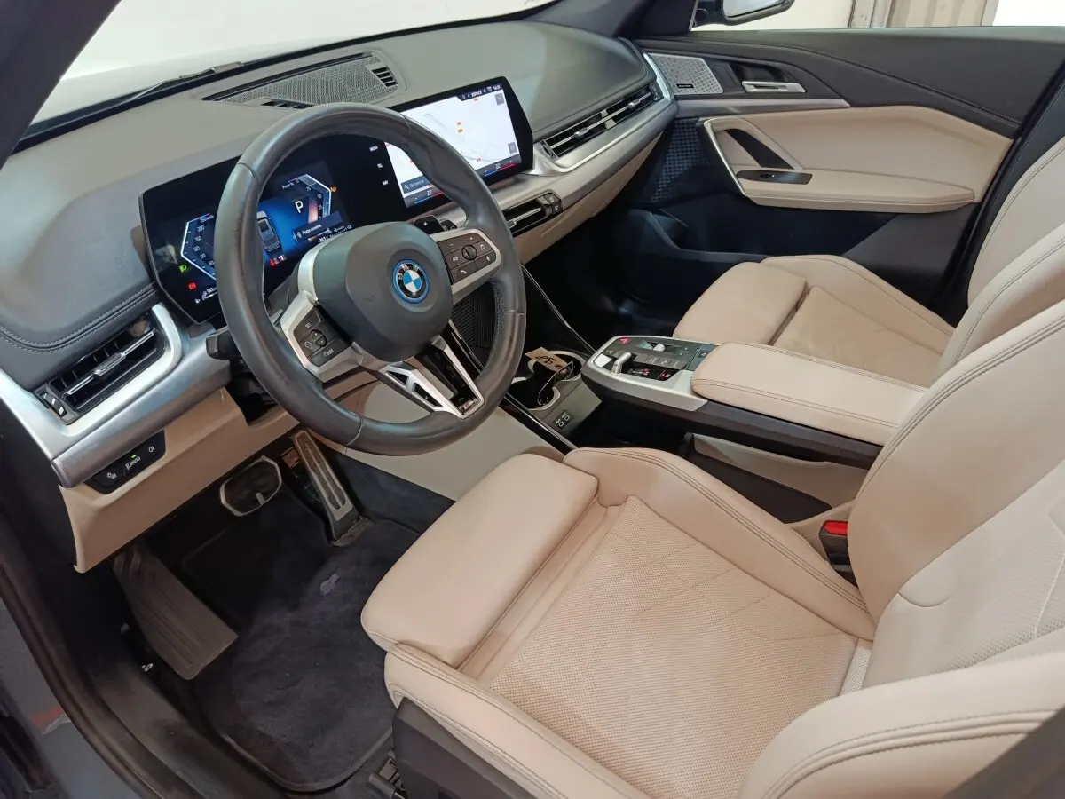 Vue intérieure côté conducteur du BMW X1 xDrive25e 2024 avec sièges cuir beige et tableau de bord digital moderne.