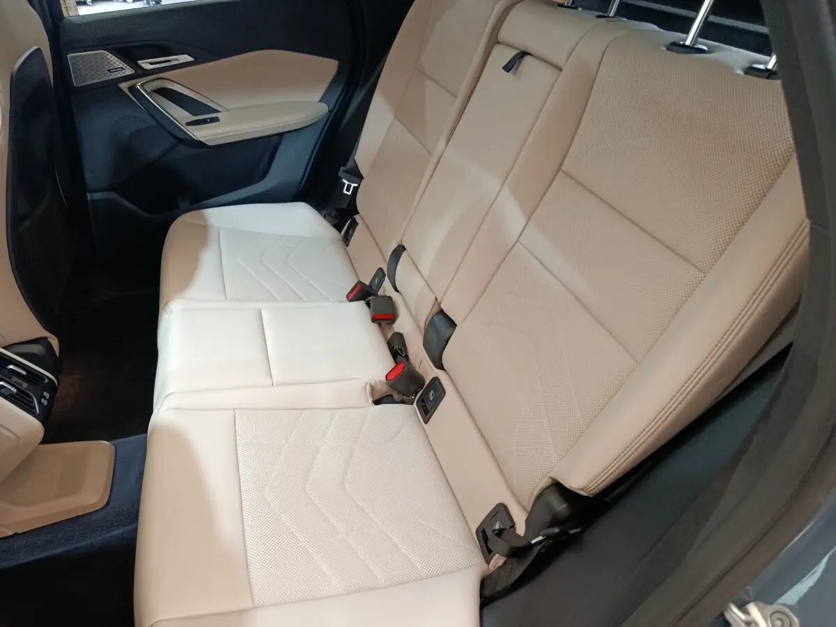Vue intérieure sur la banquette arrière beige du BMW X1 xDrive25e M Sport 2024, avec ceinture et habillage gris foncé.