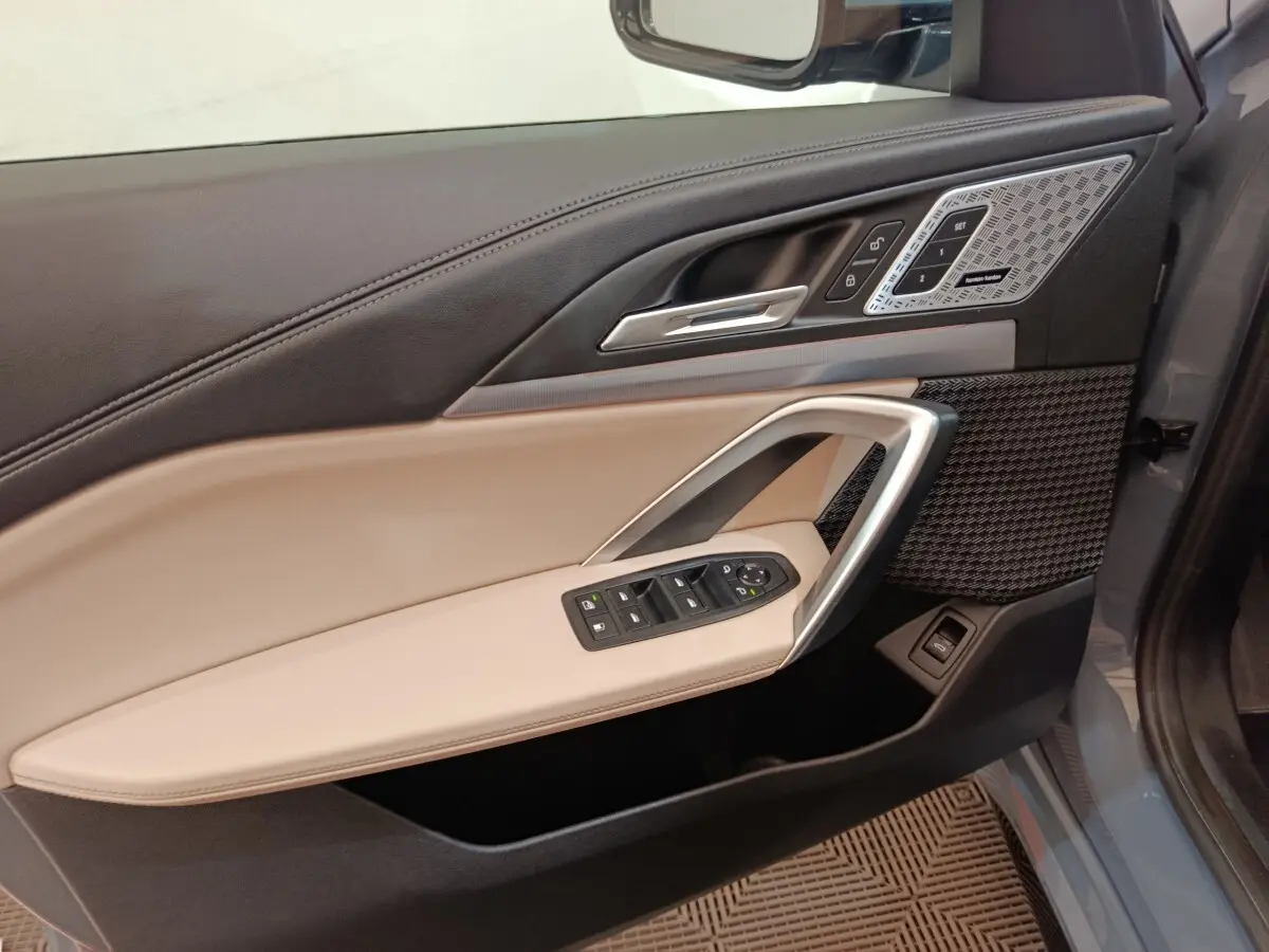 Vue intérieure côté gauche de la porte BMW X1 xDrive25e M Sport 2024, garniture beige et noire avec commandes électriques.